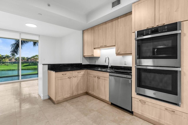 kitchen with visible vents, a water view, stainless steel appliances, light brown cabinets, and a sink