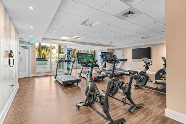 workout area with a paneled ceiling, visible vents, baseboards, and wood finished floors