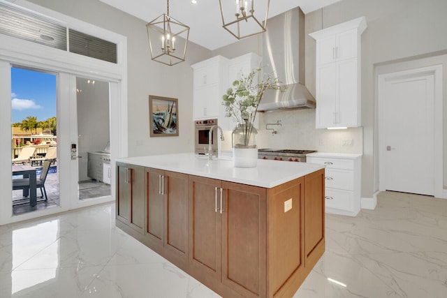 kitchen with a kitchen island with sink, white cabinets, a healthy amount of sunlight, and wall chimney range hood