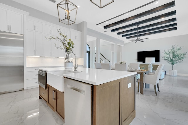 kitchen with stainless steel appliances, pendant lighting, beamed ceiling, white cabinetry, and an island with sink