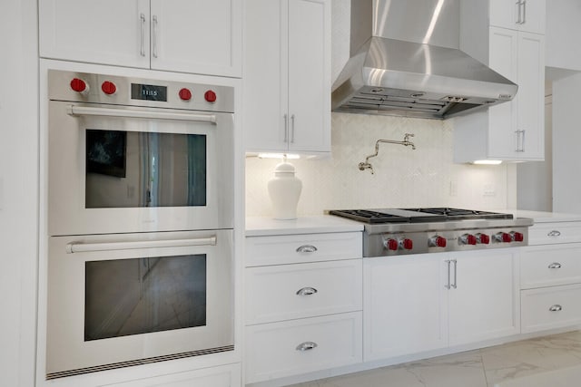 kitchen featuring stainless steel appliances, white cabinetry, tasteful backsplash, and wall chimney exhaust hood