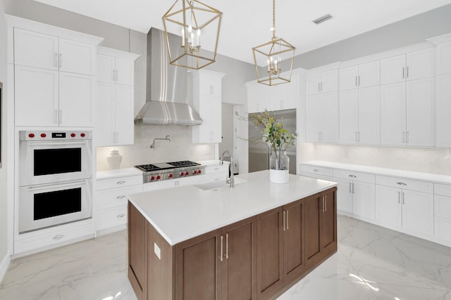 kitchen featuring stainless steel gas stovetop, white double oven, wall chimney range hood, white cabinetry, and hanging light fixtures