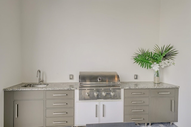 kitchen with light stone countertops, gray cabinetry, and sink