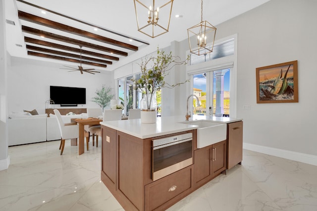 kitchen featuring sink, beamed ceiling, pendant lighting, a center island with sink, and ceiling fan with notable chandelier