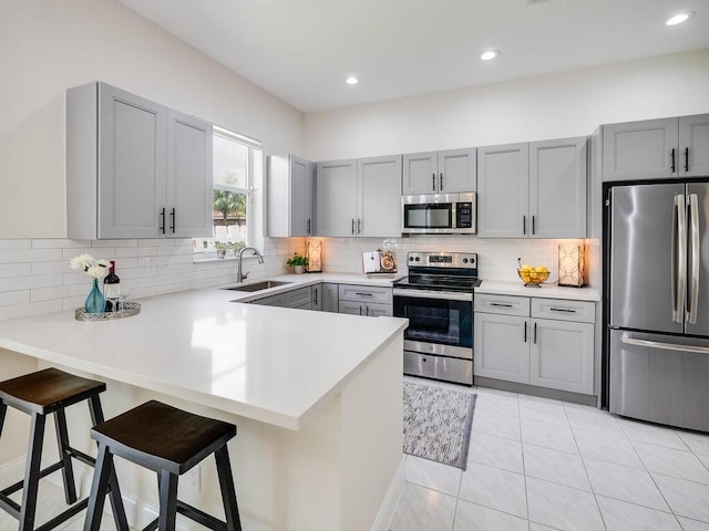 kitchen with kitchen peninsula, a kitchen breakfast bar, gray cabinetry, stainless steel appliances, and sink