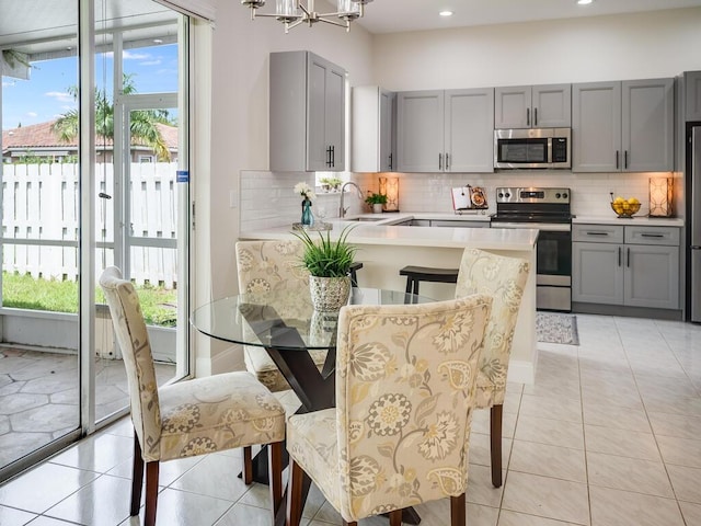 kitchen with gray cabinetry, sink, decorative backsplash, light tile patterned floors, and appliances with stainless steel finishes