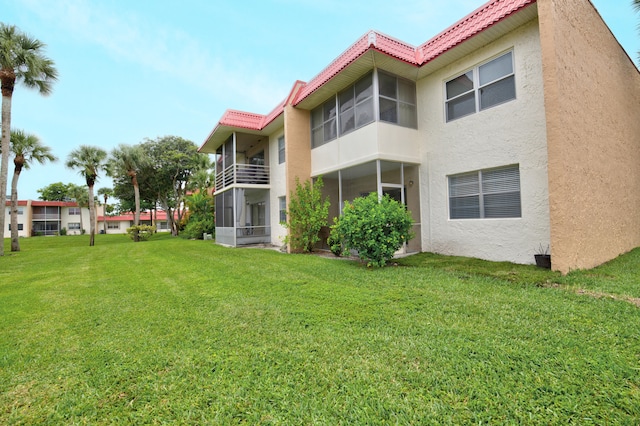 rear view of house featuring a lawn, a balcony, and a sunroom