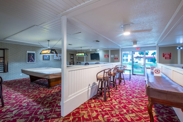 playroom featuring a textured ceiling, indoor bar, billiards, ceiling fan, and brick wall