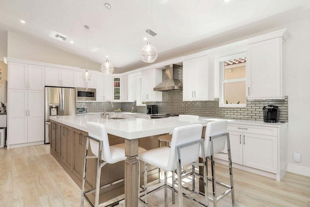 kitchen with a center island with sink, appliances with stainless steel finishes, wall chimney range hood, and white cabinetry