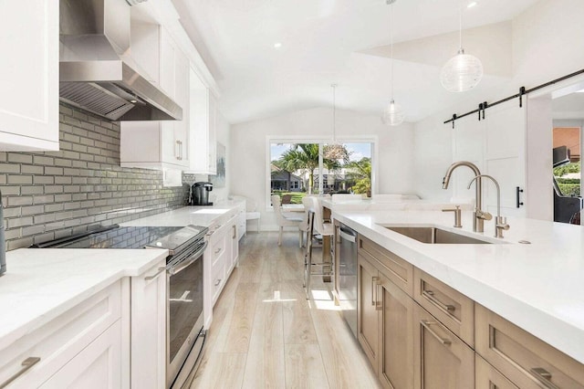 kitchen with hanging light fixtures, a healthy amount of sunlight, a barn door, stainless steel appliances, and wall chimney range hood