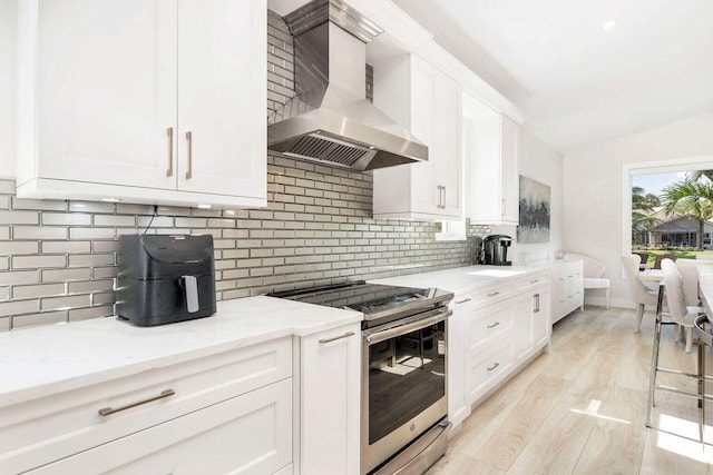 kitchen featuring wall chimney range hood, lofted ceiling, white cabinetry, and stainless steel range with electric stovetop