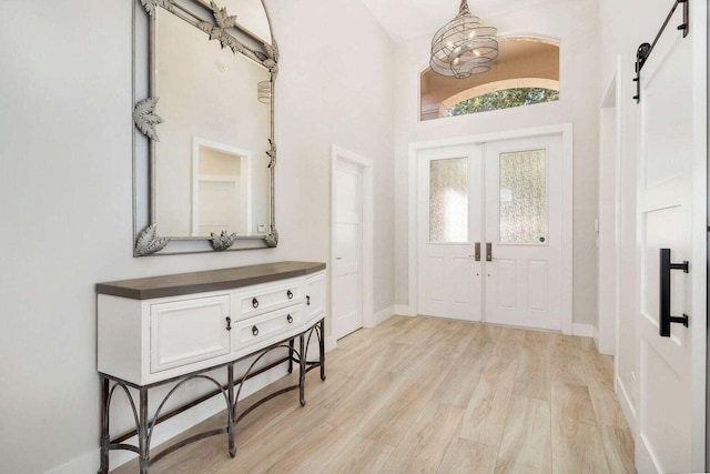 entrance foyer with a barn door, a high ceiling, a notable chandelier, and light hardwood / wood-style floors