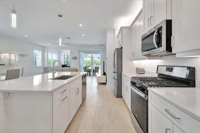 kitchen with white cabinets, a kitchen island with sink, hanging light fixtures, and appliances with stainless steel finishes