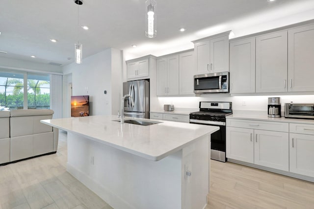 kitchen featuring sink, an island with sink, decorative light fixtures, appliances with stainless steel finishes, and light wood-type flooring