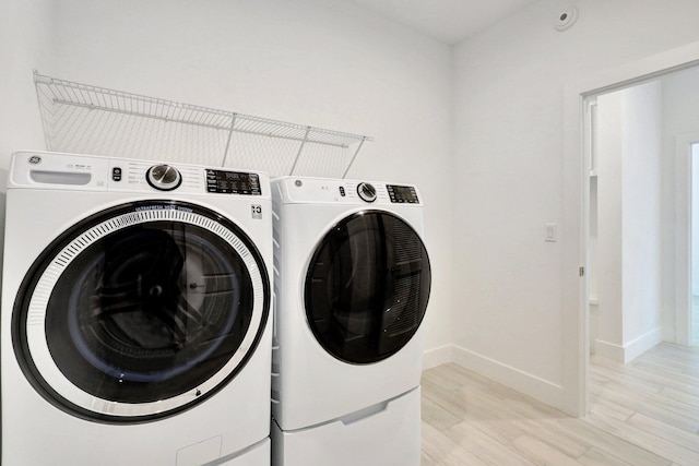 clothes washing area with washer and clothes dryer and light wood-type flooring