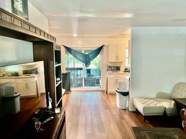 interior space with a textured ceiling, white cabinetry, and light hardwood / wood-style floors