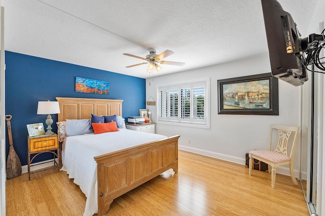 bedroom with a textured ceiling, light wood-type flooring, a ceiling fan, and baseboards