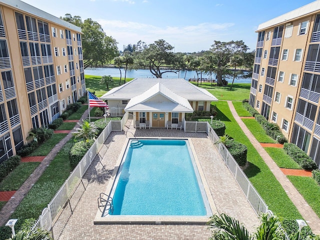 community pool with a storage structure, a water view, a fenced backyard, and an outbuilding