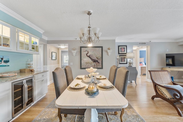 dining area with a textured ceiling, beverage cooler, light hardwood / wood-style flooring, and a notable chandelier