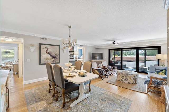 dining area featuring light wood-type flooring, ceiling fan with notable chandelier, crown molding, and a textured ceiling