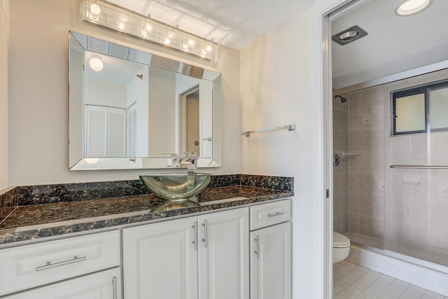 bathroom with tile patterned flooring, vanity, a tile shower, a textured ceiling, and toilet