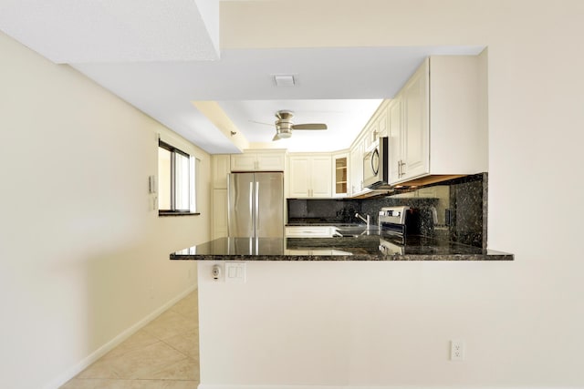 kitchen with light tile patterned flooring, tasteful backsplash, dark stone countertops, appliances with stainless steel finishes, and kitchen peninsula