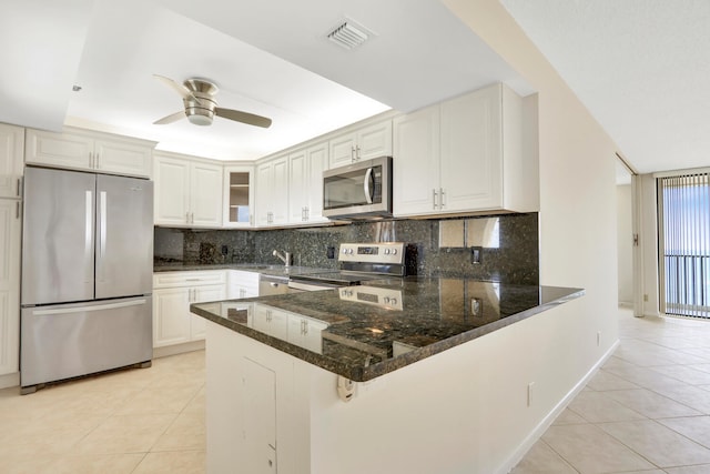 kitchen featuring white cabinets, dark stone countertops, kitchen peninsula, and stainless steel appliances