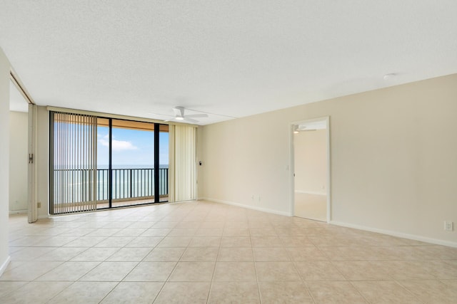 spare room with a textured ceiling, floor to ceiling windows, ceiling fan, and a water view