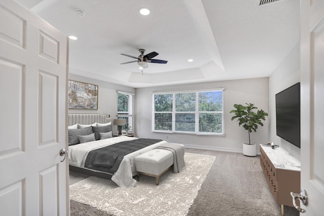 bedroom with ceiling fan, a tray ceiling, and light carpet