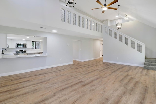 unfurnished living room with a high ceiling, wood-type flooring, ceiling fan, and sink