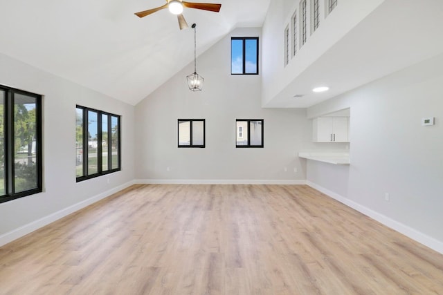 unfurnished living room featuring ceiling fan with notable chandelier, high vaulted ceiling, and light hardwood / wood-style floors