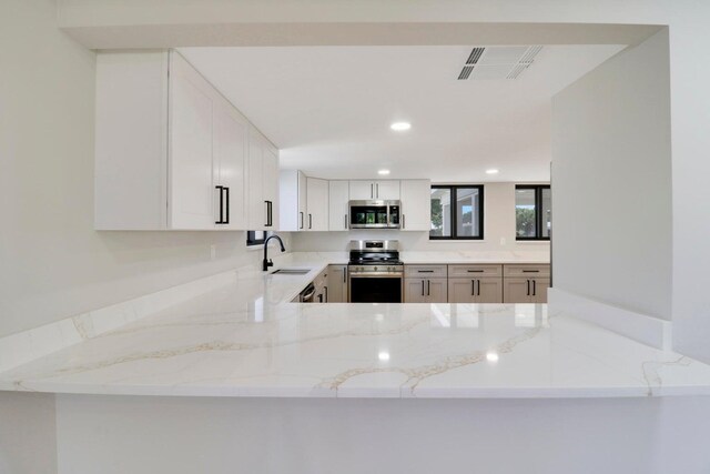 kitchen featuring appliances with stainless steel finishes, light stone counters, white cabinetry, and sink