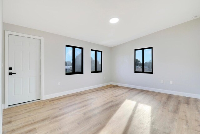 spare room with lofted ceiling, a healthy amount of sunlight, and light hardwood / wood-style floors