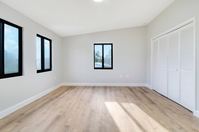 unfurnished bedroom with multiple windows, lofted ceiling, light hardwood / wood-style flooring, and a closet