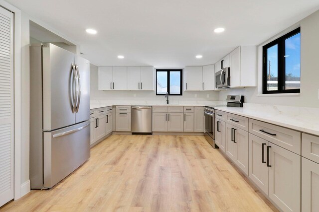 kitchen featuring a wealth of natural light, stainless steel appliances, light stone counters, and light wood-type flooring