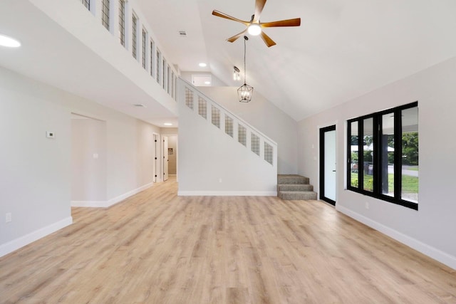 unfurnished living room featuring ceiling fan with notable chandelier, high vaulted ceiling, and light hardwood / wood-style flooring