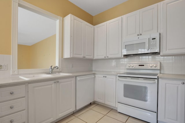 kitchen with white appliances, backsplash, sink, light tile patterned flooring, and white cabinetry