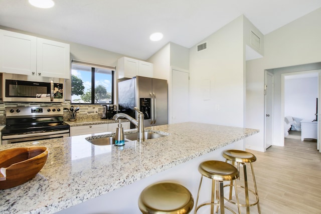 kitchen with light hardwood / wood-style floors, a breakfast bar, stainless steel appliances, sink, and light stone counters