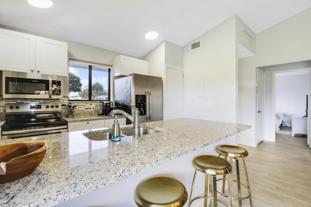 kitchen with visible vents, a breakfast bar, a sink, light stone counters, and appliances with stainless steel finishes