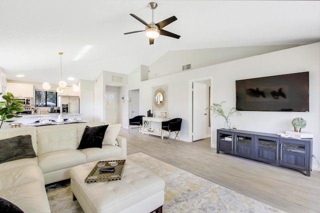 living room with vaulted ceiling, ceiling fan with notable chandelier, and light wood-type flooring