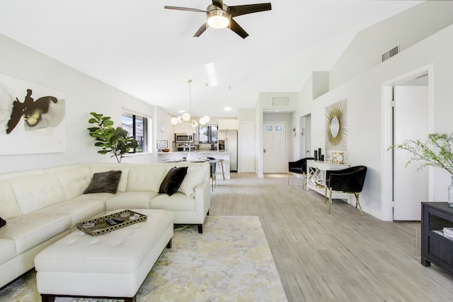 living area featuring lofted ceiling, ceiling fan with notable chandelier, visible vents, and light wood-type flooring