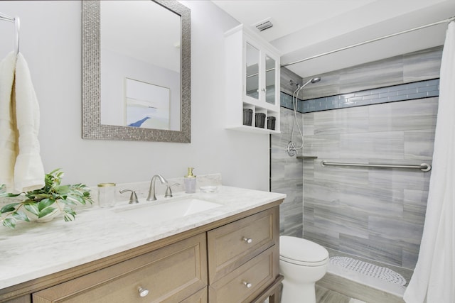 bathroom with vanity, toilet, visible vents, and tiled shower