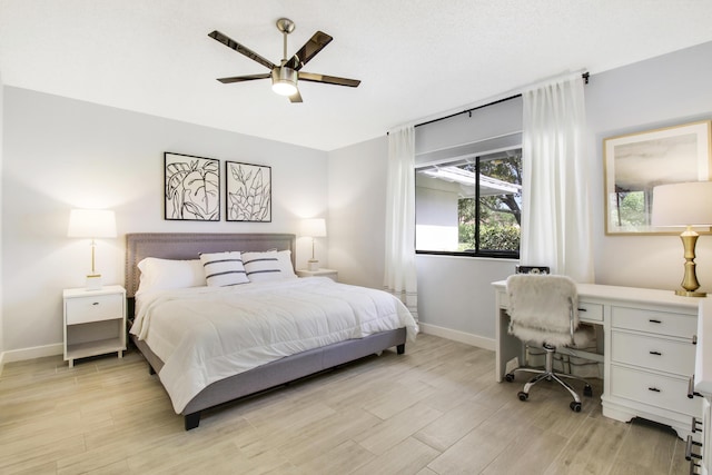 bedroom featuring light wood-style flooring, a ceiling fan, baseboards, and built in study area