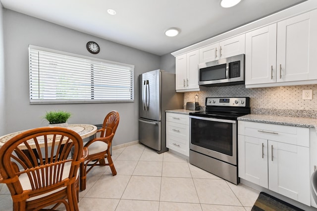 kitchen with backsplash, white cabinets, light tile patterned floors, appliances with stainless steel finishes, and light stone counters