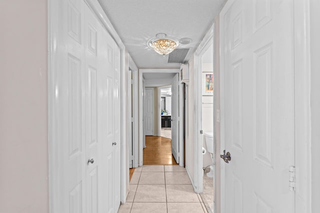 corridor with light tile patterned floors, a chandelier, and a textured ceiling