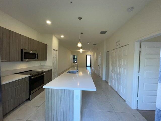 kitchen with sink, stainless steel appliances, decorative light fixtures, a kitchen island with sink, and light tile patterned flooring