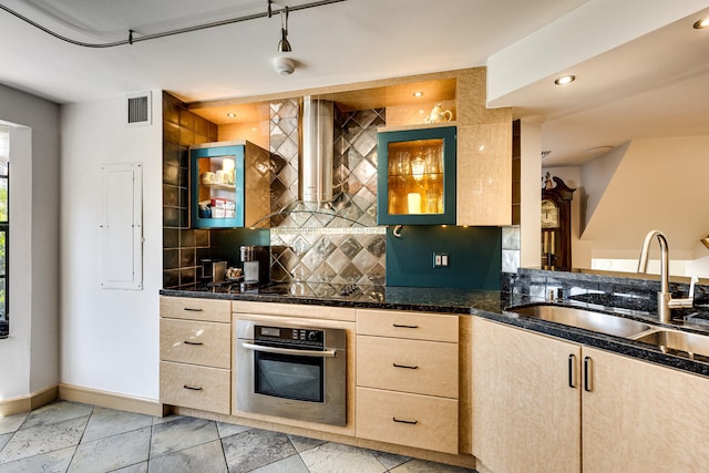 kitchen featuring sink, stainless steel oven, decorative backsplash, wall chimney exhaust hood, and light brown cabinets