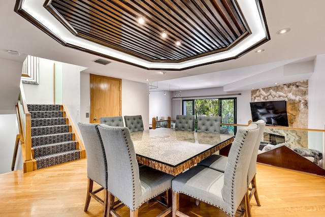 dining room with a premium fireplace, a raised ceiling, and light hardwood / wood-style flooring