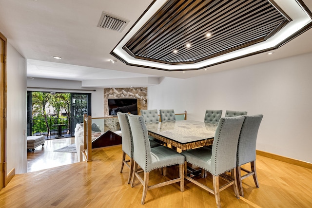 dining space with light hardwood / wood-style flooring, a high end fireplace, and a raised ceiling