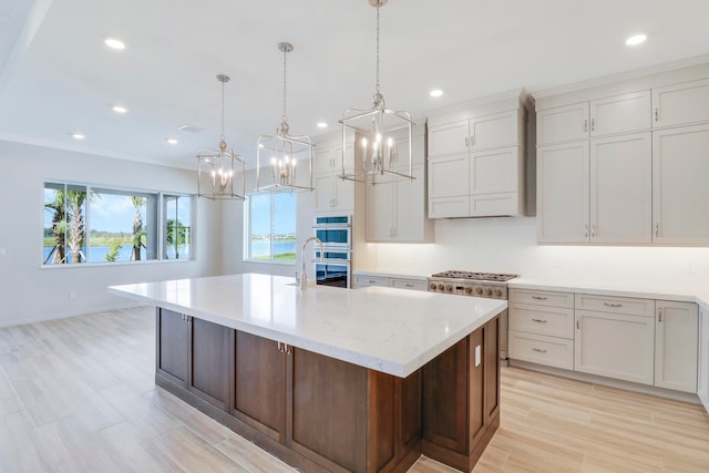 kitchen with a large island with sink, appliances with stainless steel finishes, pendant lighting, wall chimney range hood, and white cabinets